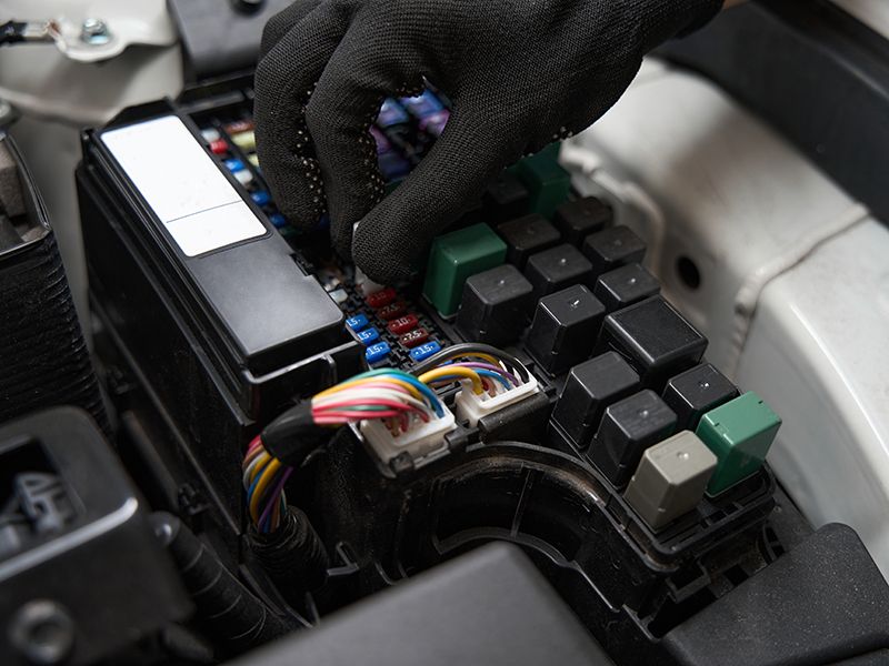 Primer plano de las manos de un mecánico que revisa el fusible en el sistema eléctrico del automóvil, el hombre trabaja con guantes protectores